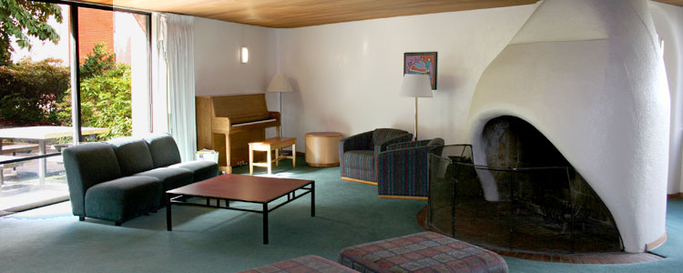 A fireplace, seating area and upright piano in the main lounge of Nash Hall