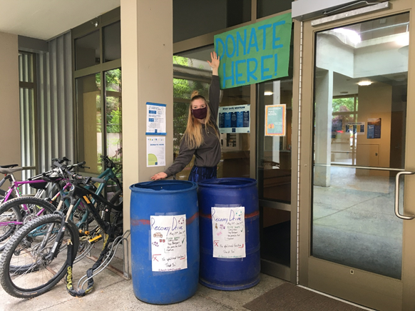 A student displays two blue bins with a sign reading "Donate Here!"