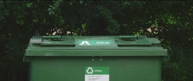 Photo of a green recycling bin against a row of trees