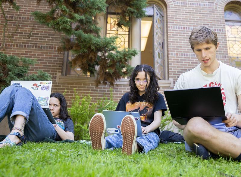 Three students on their laptops in the grass 
