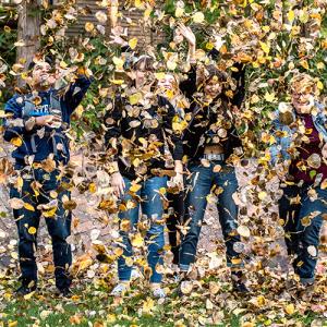 A group of students throw a pile of leaves into the air in the Fairhaven courtyard