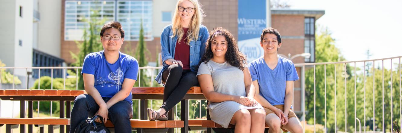 Four Students sit on a bench with the Viking union in the background