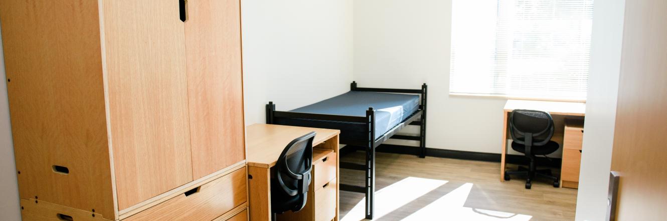 A brand new, clean dorm room with beds, desks, and light shining through the window